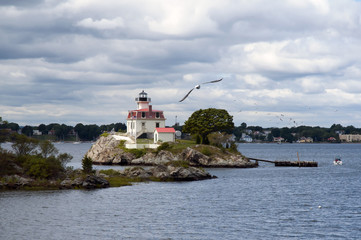 Sun illuminating Pomham Rocks lighthouse after stormy weather in Rhode Island as seagull flies in...