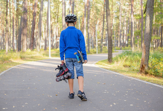 Little boy carrying skateboard and roller skates