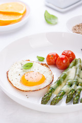 Fried egg with asparagus and tomatoes on a white plate with blue napkin. ..