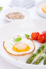 Fried egg with asparagus and tomatoes on a white plate with blue napkin. closeup..