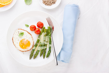Fried egg with asparagus and tomatoes on a white plate with blue napkin.
