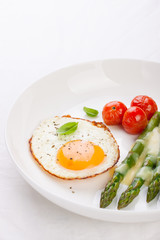 Fried egg with asparagus and tomatoes on a white plate with blue napkin. .