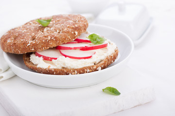 Sandwich with wholewheat bread, cottage cheese, radish and basil on a white plate, closeup, selective focus..