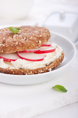 Sandwich with wholewheat bread, cottage cheese, radish and basil on a white plate, closeup, selective focus..