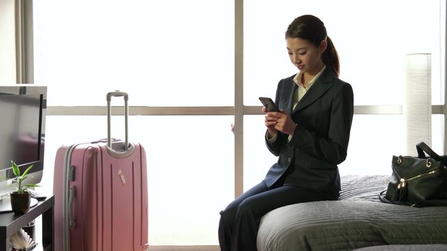 Business travel, people traveling, working in hotel room, Japanese female manager. Asian businesswoman, girl, woman at work, texting message with smartphone, mobile phone, telephone for email internet