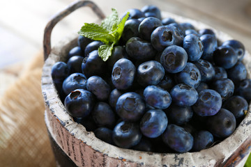Tasty ripe blueberries with green leaves in bucket on table close up