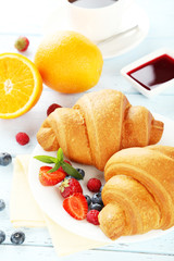 Fresh tasty croissants with berries on blue wooden background