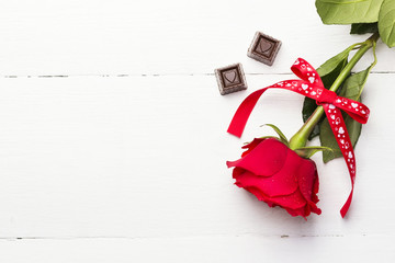 Red rose, chocolates on a white wooden background