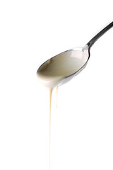 Condensed milk pouring from a spoon, isolated on white
