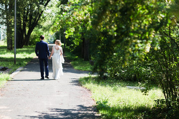 Fototapeta premium A happy young newly married couple walking in the park. Beautiful bride and groom kissing in the woods.