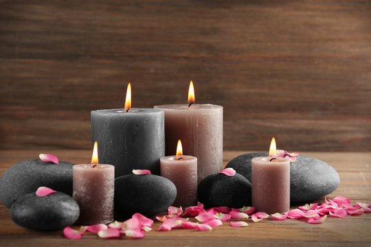 Alight wax grey candle with flower petals and pebbles on wooden background