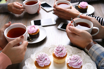 Four hands with smart phones holding  cups with tea, on wooden table background