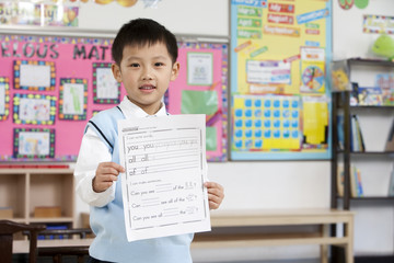 Young boy proudly holding up his work in class