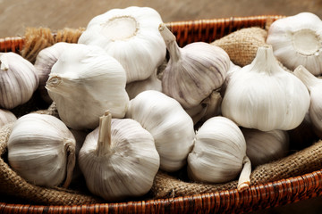 Garlic in wicker bowl on wooden background, close up