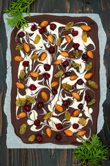 Holiday chocolate bark with dried fruits and nuts on a dark wood background. Top view. Dessert recipe for judaic holiday Tu Bishvat