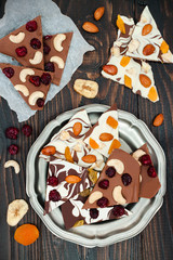 Holiday chocolate bark with dried fruits and nuts on a dark wood background. Top view. Dessert recipe for judaic holiday Tu Bishvat