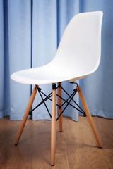 Stylish white chair on blue curtains background