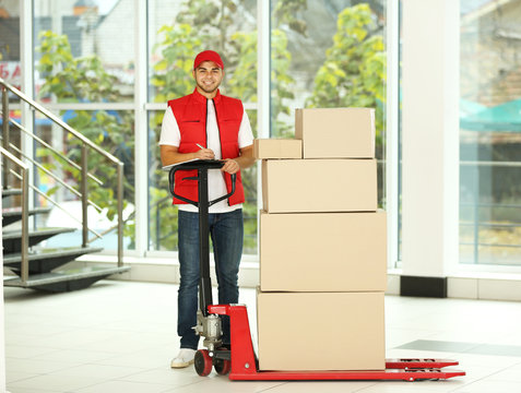 Delivery Concept - Postman In Red Uniform With Parcels On Dolly