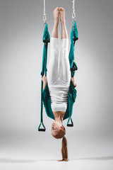 Young woman practices different inversion aerial yoga with a hammock in a white studio. Concept of a mental and physical health and harmony living