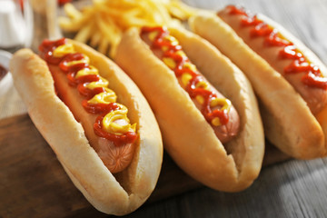 Tasty hot-dogs with French chips, spices and vegetables on wooden background, close up