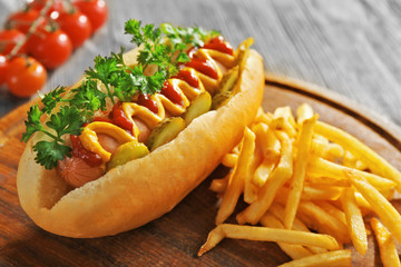 Delicious hot-dog with French fries and vegetables on wooden background