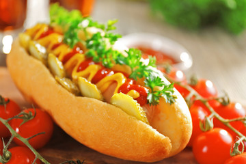 Delicious hot-dog with tomatoes and ketchup on wooden chopping board, close up