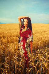 Smiling Young woman with ornamental dress standing on a wheat field with sunset. Natural background..