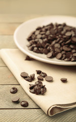 Chocolate morsels on plate, on wooden board