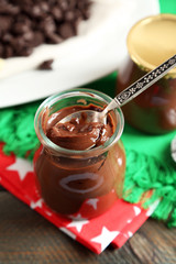 Chocolate dessert in small glass jars and morsels on plate, on wooden background