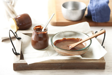 Melted chocolate on glass bowl on tray, on wooden background