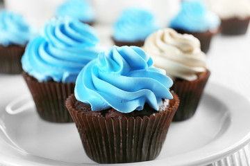 Chocolate cupcakes with colourful cream on white saucer, close up