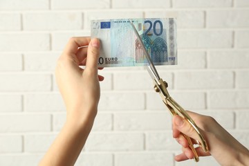 Hands with scissors cutting money on white brick wall background