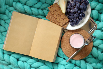 Open book, plaid and glass of yogurt  on sofa. Top view
