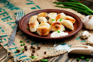 Ukrainian and china national cuisine , fried dumplings with meat or potatoes with sour cream or mayonnaise , green onions, garlic , pepper and spices on a wooden background