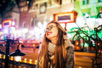 Street portrait of smiling beautiful young woman with glasses on the festive Christmas fair. Model smile  at camera.  Christmas market
