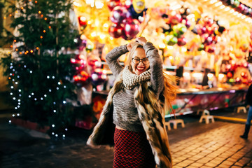 Street portrait of smiling beautiful young woman on the festive Christmas fair. Model looking at camera.  Christmas market