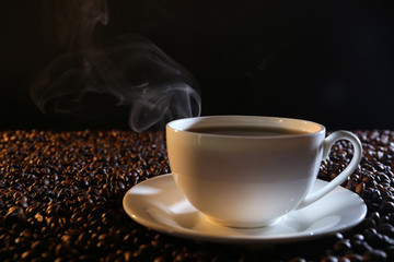 Cup of hot coffee among coffee beans on dark background