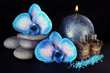 Spa set. Beautiful blue orchid with pile of pebbles, candle, sea salt and aroma oil on black background