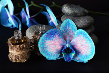 Beautiful blue orchid with pile of pebbles and candle on black background, close up