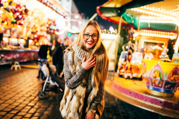 Street portrait of smiling beautiful young woman on the festive Christmas fair. Model looking at...
