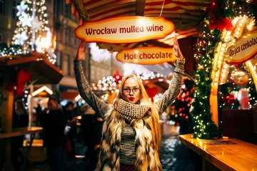 Street portrait of smiling beautiful young woman on the festive Christmas fair. Model looking at camera.  Christmas market