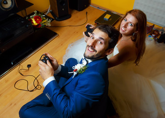 bride and groom playing together videogames with joysticks - gaming and wedding concept.