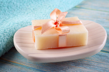 Soap with ribbon on a dish over wooden background, close up