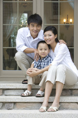 A family of three sitting in front of a house