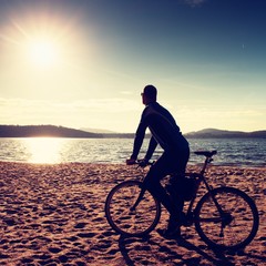 Young man cyclist silhouette on blue sky and sunset background on the beach. End of season at lake.