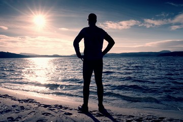 Silhouette of person in sportswear and short hair  on beach see into Sun above sea
