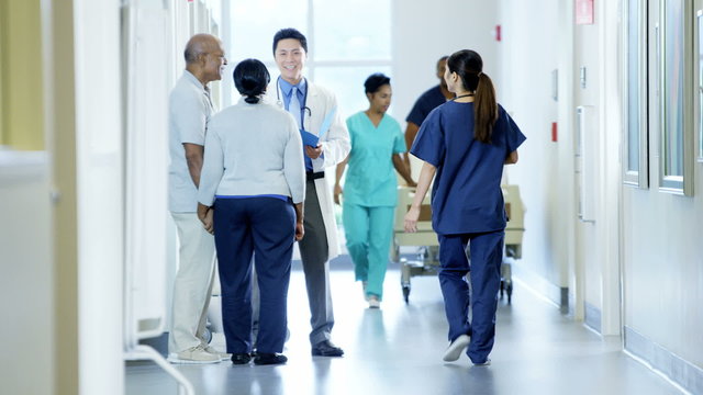 Staff of hospital work on corridor and male doctor consult with senior couple