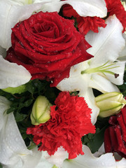 Beautiful pretty floral tribute of red roses, carnations and white lilies with rain or dew drops on the petals. 