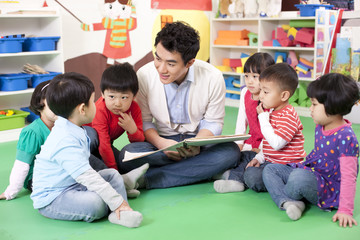 Male teacher reading picture book with cute kindergarten children