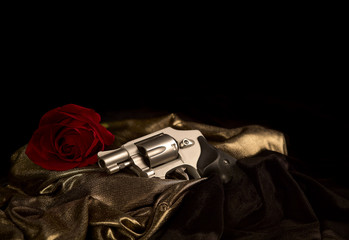 Snubnose 38 revolver laying across gold satin with a red rose and black velvet